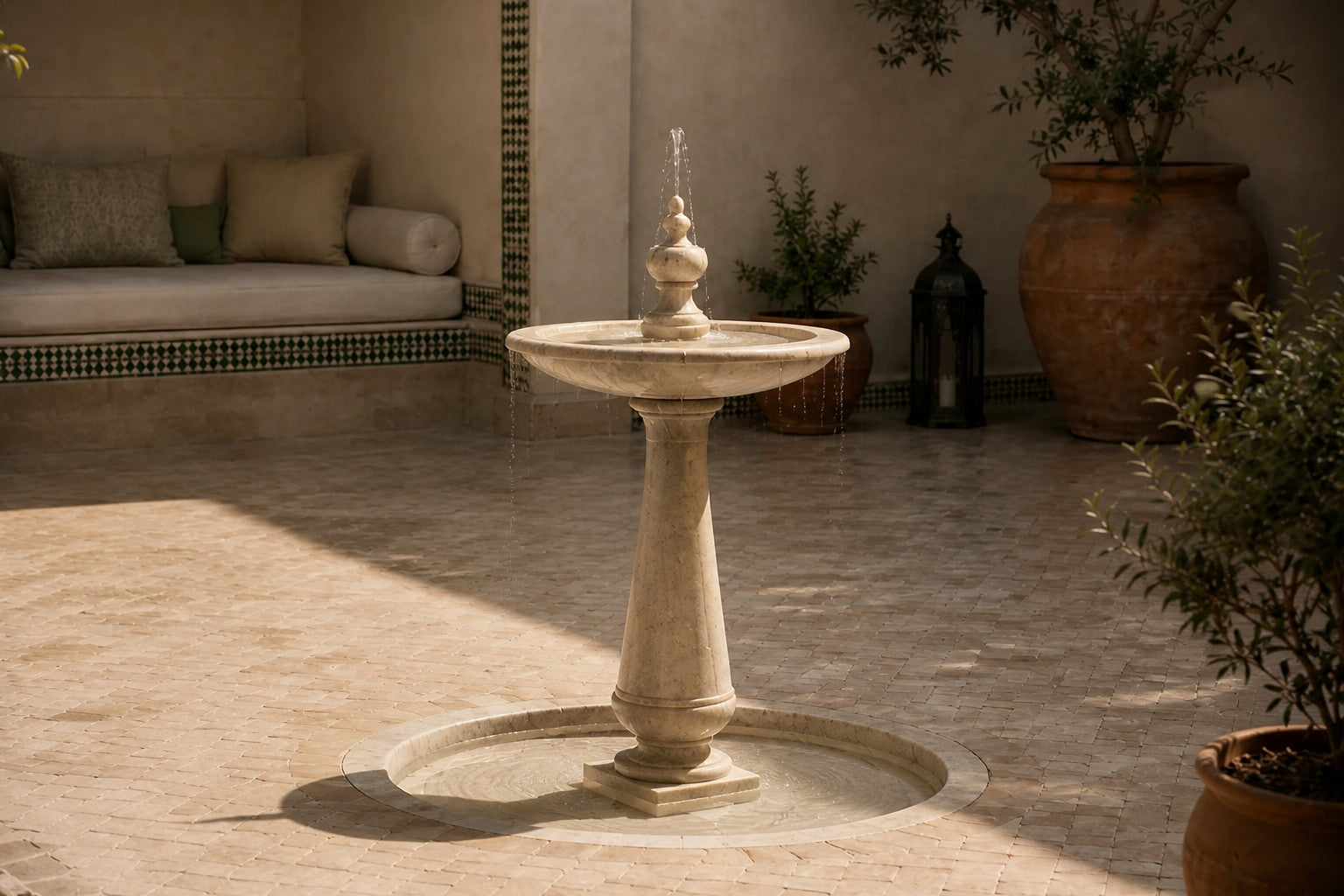 Pale limestone pedestal fountain Fontena Ø65, cream with open fossil speckle, on a pale stone floor.