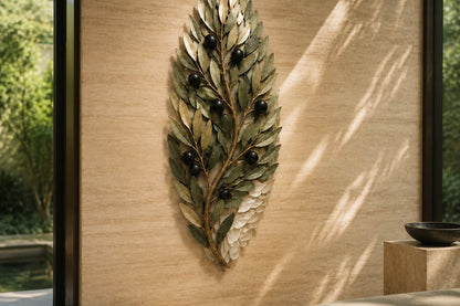 Olive green and dark bronze bronze wall sculpture Ramoscello, cast branch with individually mounted leaves and fruit, on a plaster wall.