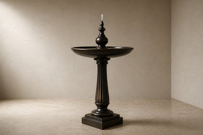 Stone pedestal fountain Goccia Ø65, near-black with a soft sheen, on a pale stone floor.
