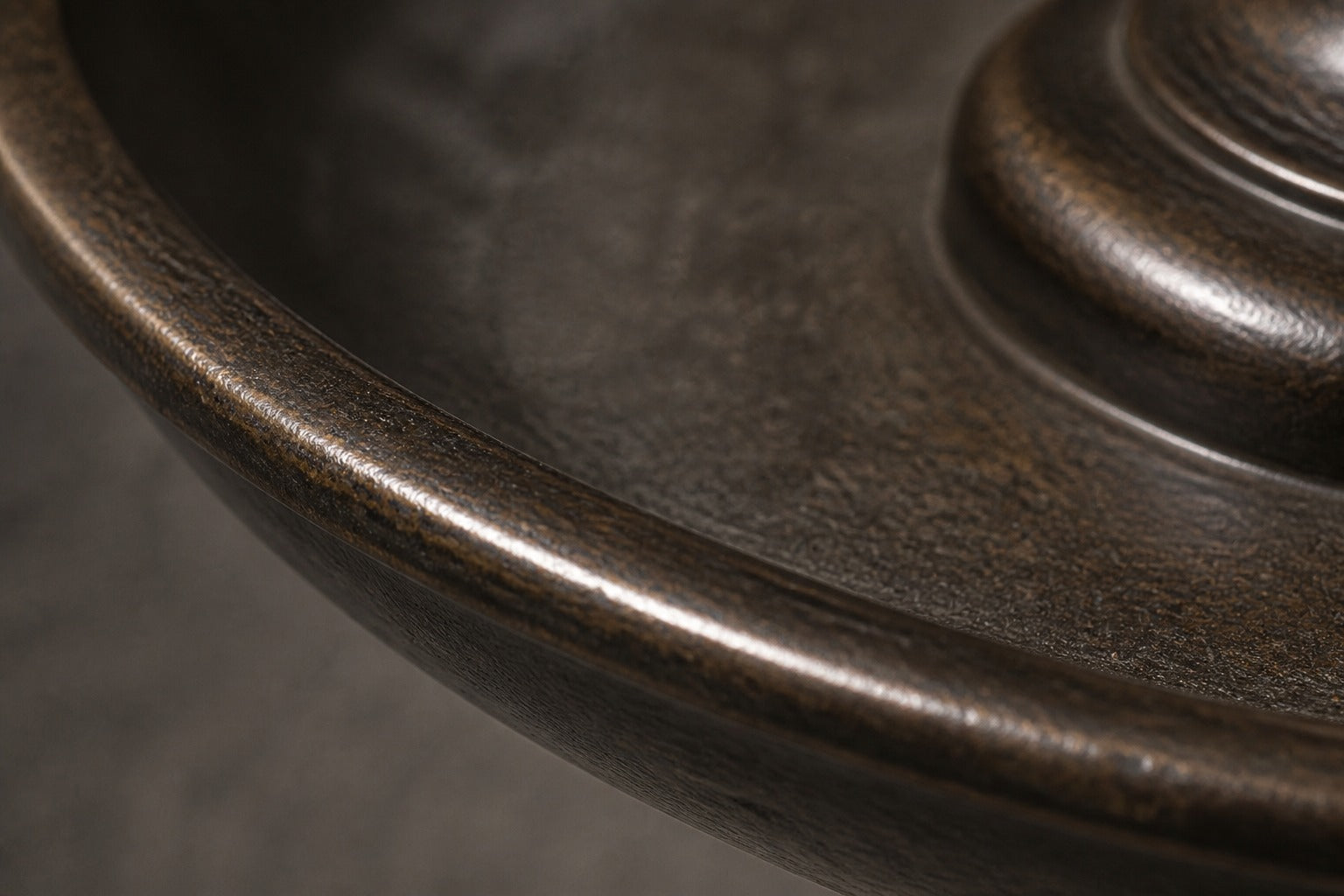 Stone pedestal fountain Goccia Ø65, near-black with a soft sheen, on a pale stone floor.