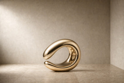 Mirror-polished brass loop sculpture Hamal knotted through itself, on a fluted cream travertine plinth.