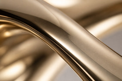 Mirror-polished brass loop sculpture Hamal knotted through itself, on a fluted cream travertine plinth.