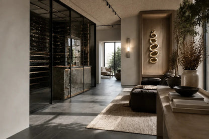 Champagne gold bronze wall sculpture Guijarro, a continuous folded ribbon swelling to a smooth belly, on a plaster wall.