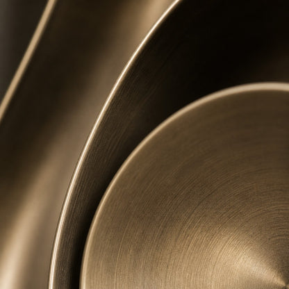 Warm brass brass wall sculpture Conca, a deep spun basin with a broad everted rim, on a plaster wall.