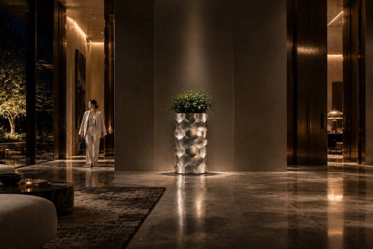 HexaFacet Stainless Steel Luxury Column Planter — 110 cm brushed stainless steel column planter with faceted honeycomb panels, the same room at night, lamps on
