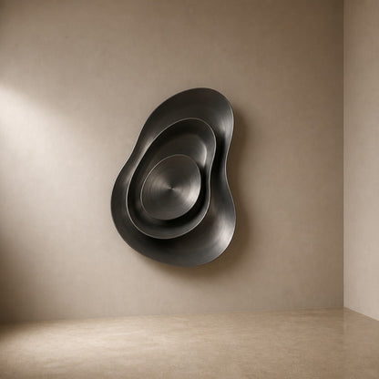 Iron grey bronze wall sculpture Roca, a cast boulder form mounted proud of a spun disc, on a plaster wall.