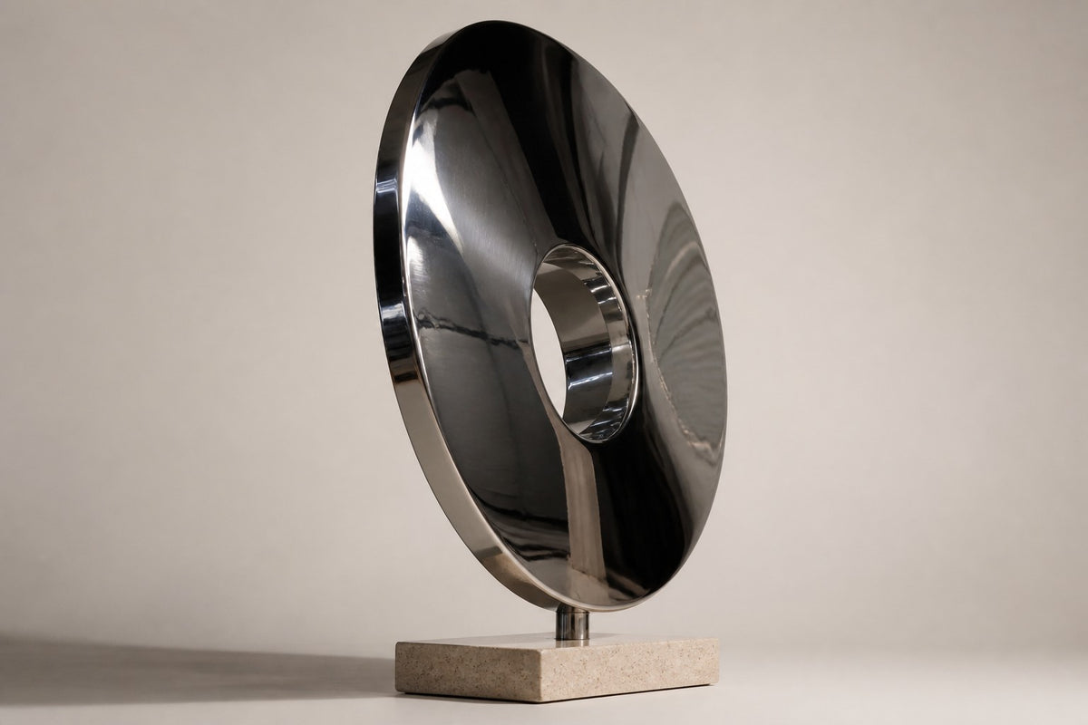 Kagami — upright dished mirror-steel disc with an off-centre hole on a travertine base, studio side angle showing its depth