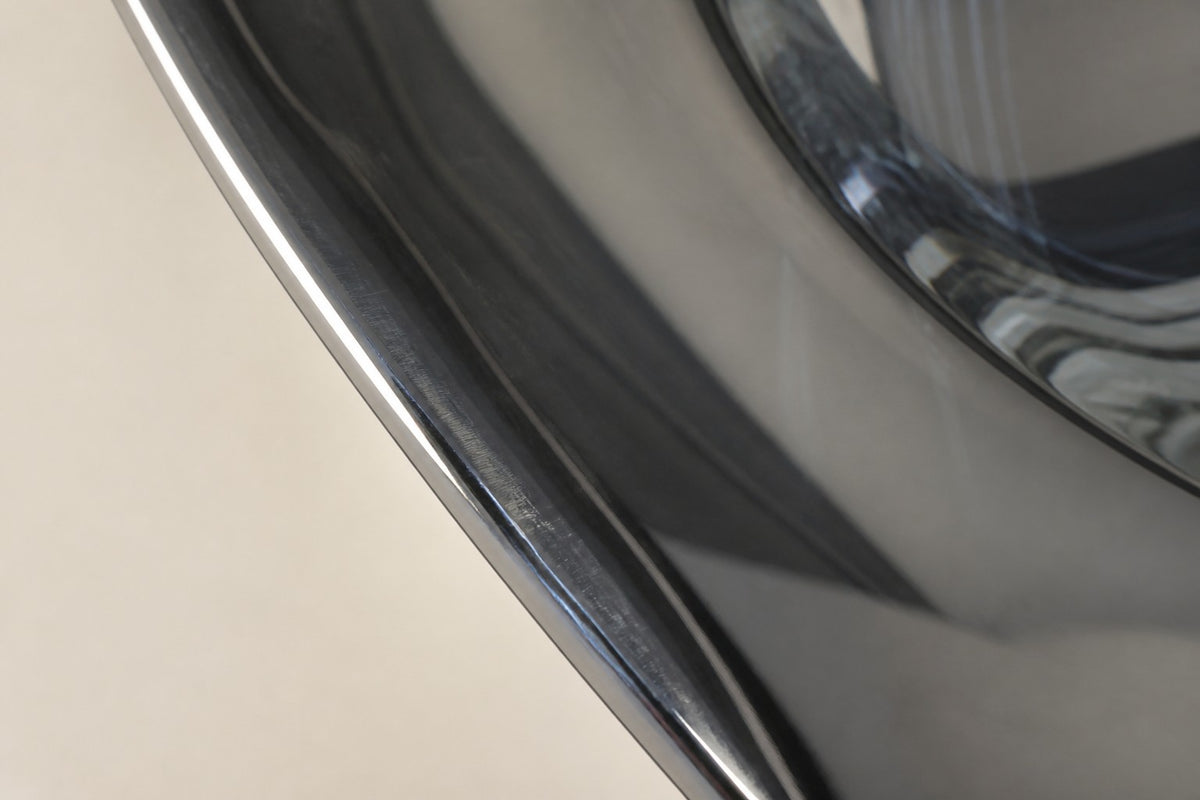 Kagami — upright dished mirror-steel disc with an off-centre hole on a travertine base, close detail of the surface and edge