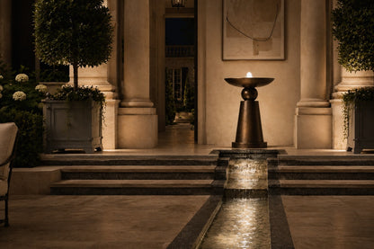 Stone pedestal fountain Kathib Ø65, pale warm stone, on a pale stone floor.