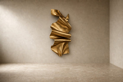 Polished gold brass wall sculpture Manto, a draped sheet caught mid-fall and fixed at one edge, on a plaster wall.