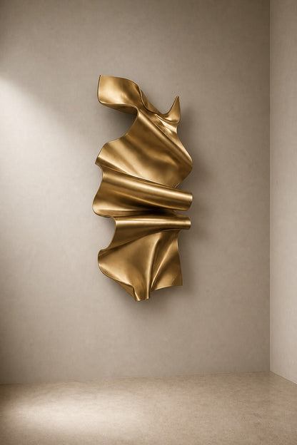 Polished gold brass wall sculpture Manto, a draped sheet caught mid-fall and fixed at one edge, on a plaster wall.
