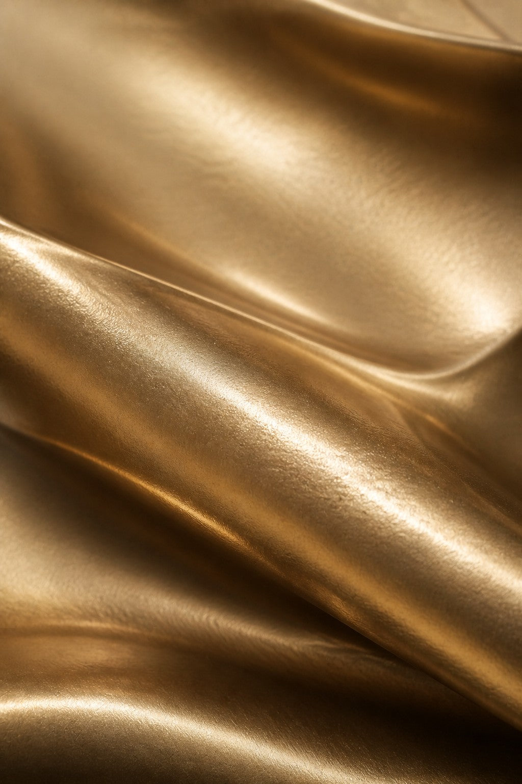 Polished gold brass wall sculpture Manto, a draped sheet caught mid-fall and fixed at one edge, on a plaster wall.