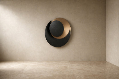 Black and warm gold bronze wall sculpture Kusuf, a matte disc overlapping a gilded crescent, on a plaster wall.