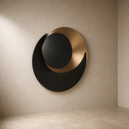 Black and warm gold bronze wall sculpture Kusuf, a matte disc overlapping a gilded crescent, on a plaster wall.
