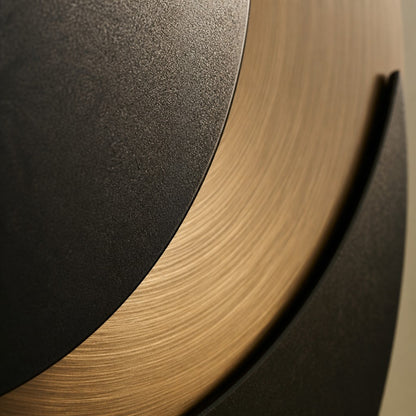Black and warm gold bronze wall sculpture Kusuf, a matte disc overlapping a gilded crescent, on a plaster wall.