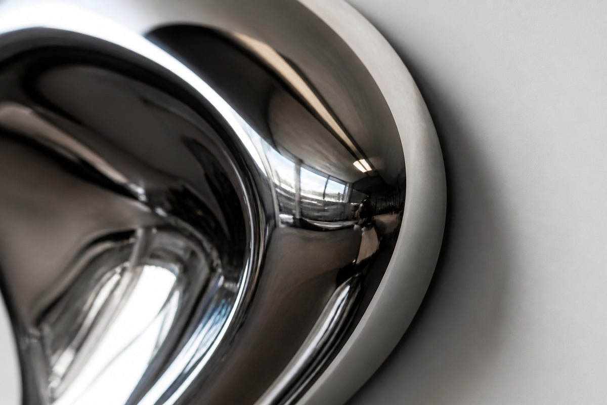 Lágrima — mirror-polished steel wall sculpture flowing down the wall into two drips, close detail of the surface and edge