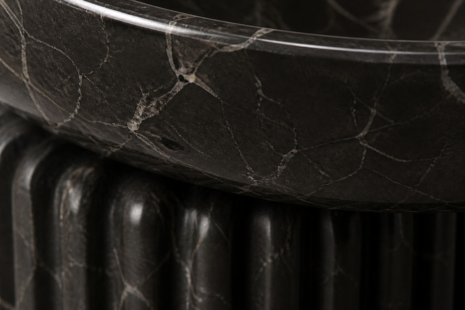 Dark marble pedestal fountain Layla Ø65, deep black with white veining, on a pale stone floor.