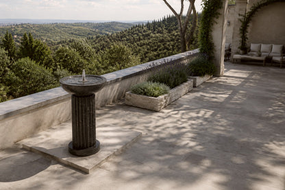 Dark marble pedestal fountain Layla Ø65, deep black with white veining, on a pale stone floor.