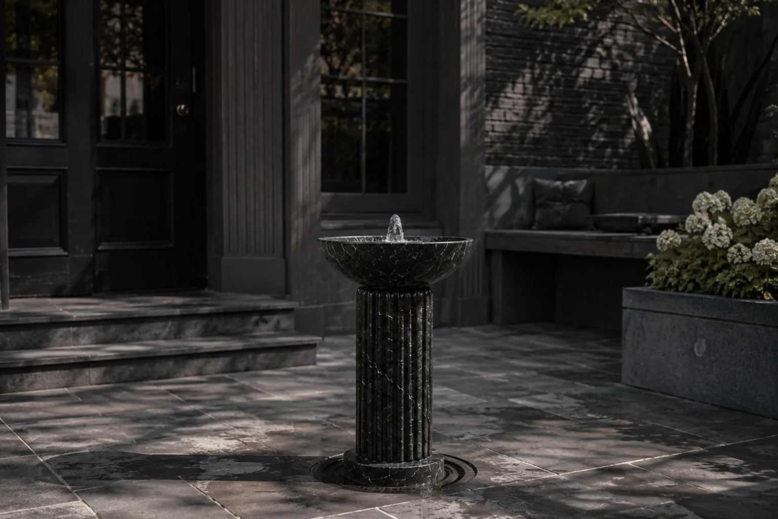 Dark marble pedestal fountain Layla Ø65, deep black with white veining, on a pale stone floor.