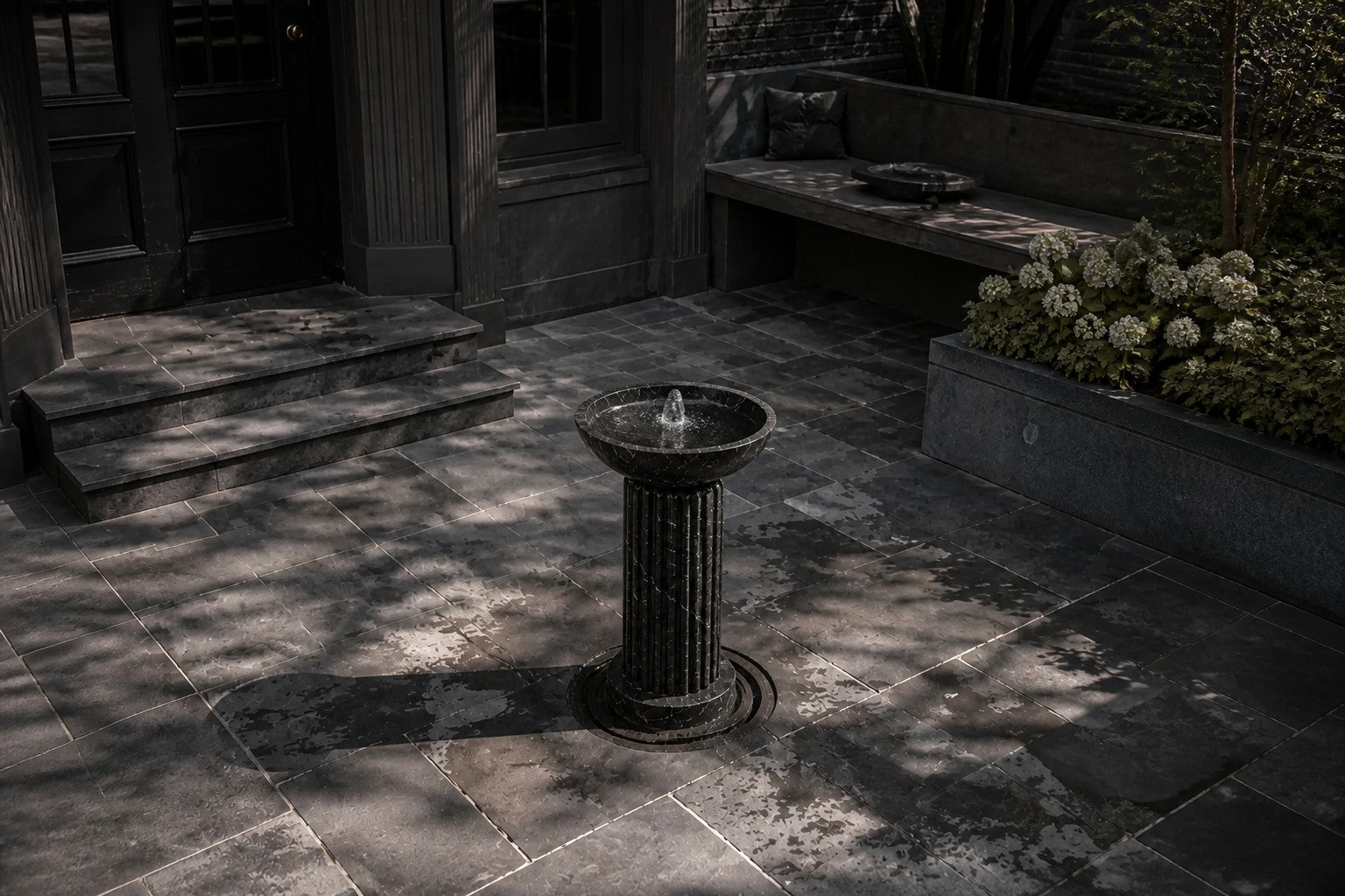 Dark marble pedestal fountain Layla Ø65, deep black with white veining, on a pale stone floor.