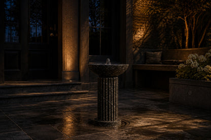 Dark marble pedestal fountain Layla Ø65, deep black with white veining, on a pale stone floor.