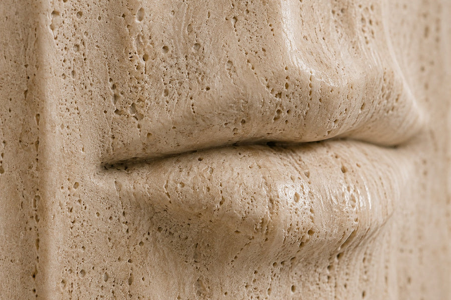 Tall cream travertine pedestal with a mouth carved in relief on one face — close detail of the surface