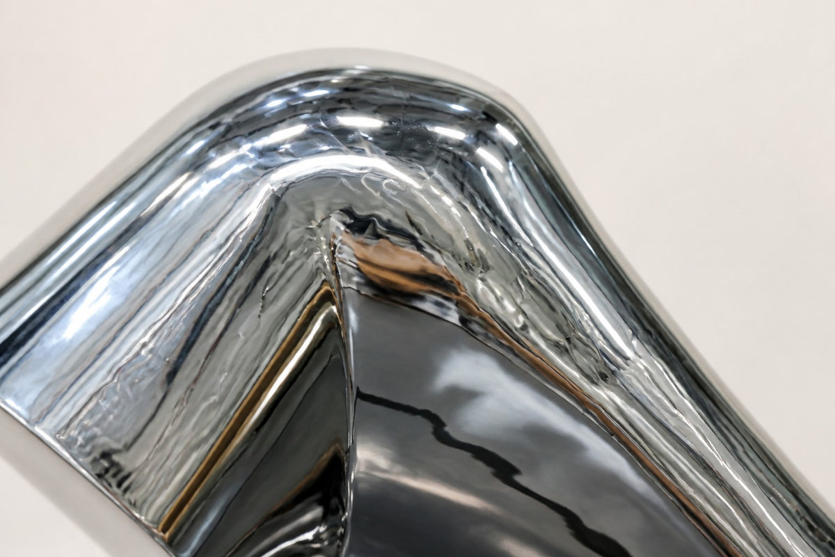 Magari — 140 cm mirror-polished steel sculpture of a bent, creased tube rising from a slim base, close studio detail of the surface and material