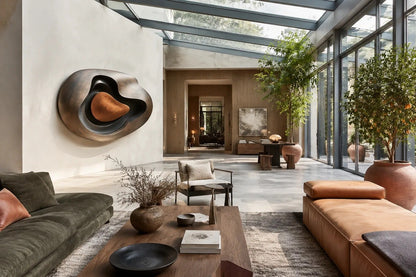 Nested ovoid bronze walls around a warm tan polished core, standing on a stone floor.