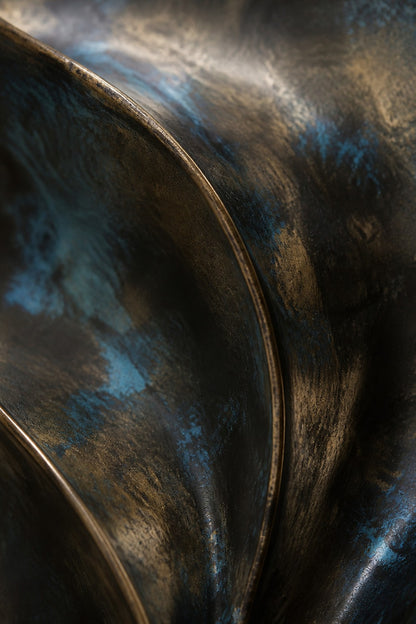 Antique bronze bronze wall sculpture Cuna, nested open ovals cradling a polished core, on a plaster wall.