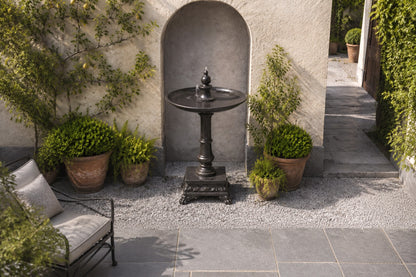 Stone pedestal fountain Mirala Ø65, dark charcoal, on a pale stone floor.