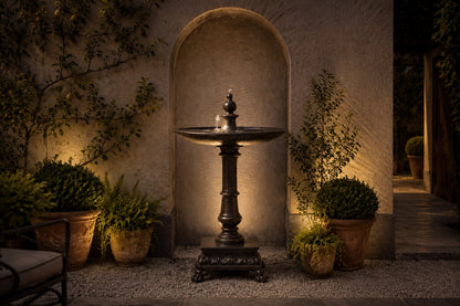 Stone pedestal fountain Mirala Ø65, dark charcoal, on a pale stone floor.