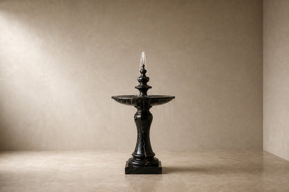 Stone pedestal fountain Nasima Ø65, black with gold and amber veining, on a pale stone floor.