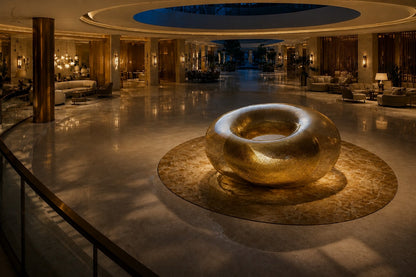 Woven brass wire torus sculpture Nunki Ø120, reading as solid gold where the mesh doubles and open gauze at the edges.