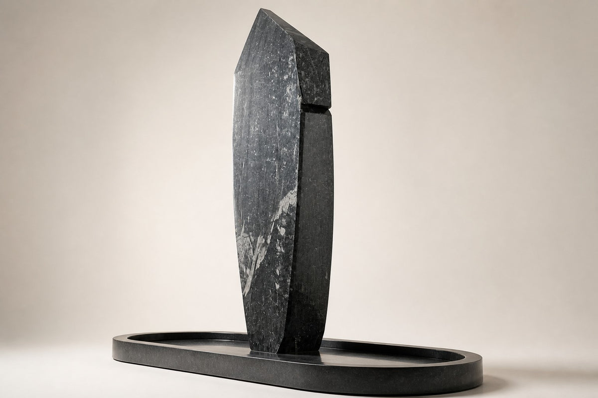 Obelisk Veil — 320 cm dark veined marble obelisk water feature in an oval stone basin, three-quarter studio view showing its profile