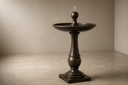 Stone pedestal fountain Ondala Ø65, warm mottled bronze, on a pale stone floor.