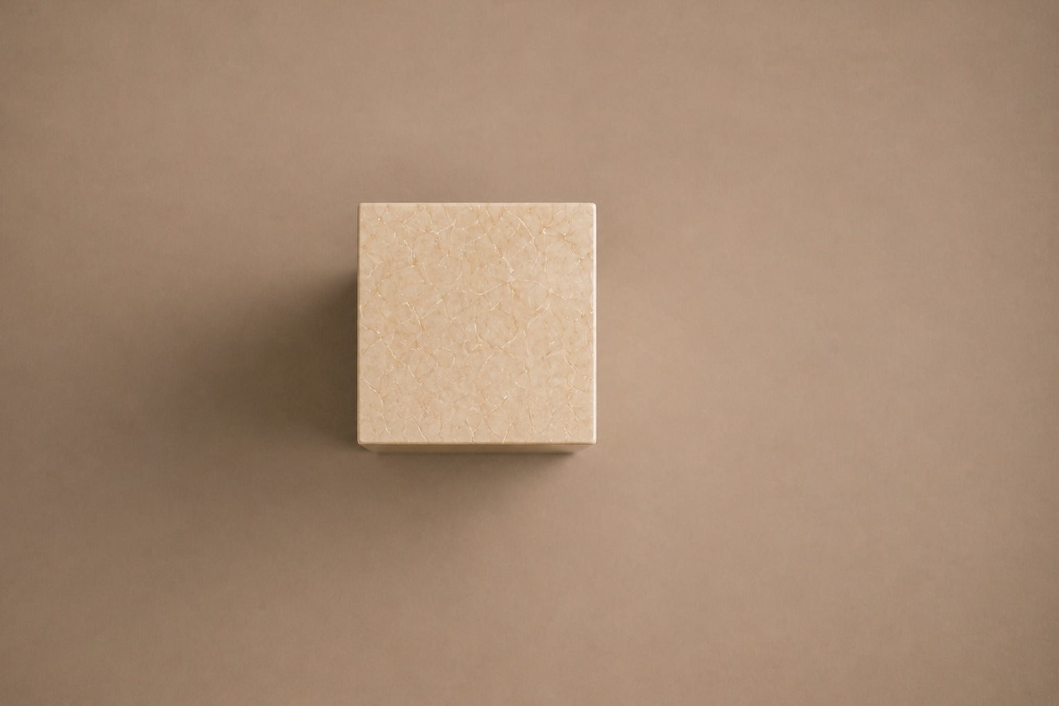 Tall cream Crema Marfil marble pedestal with a closed eye carved in shallow relief on one face.