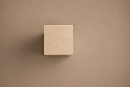 Tall cream Crema Marfil marble pedestal with a closed eye carved in shallow relief on one face.