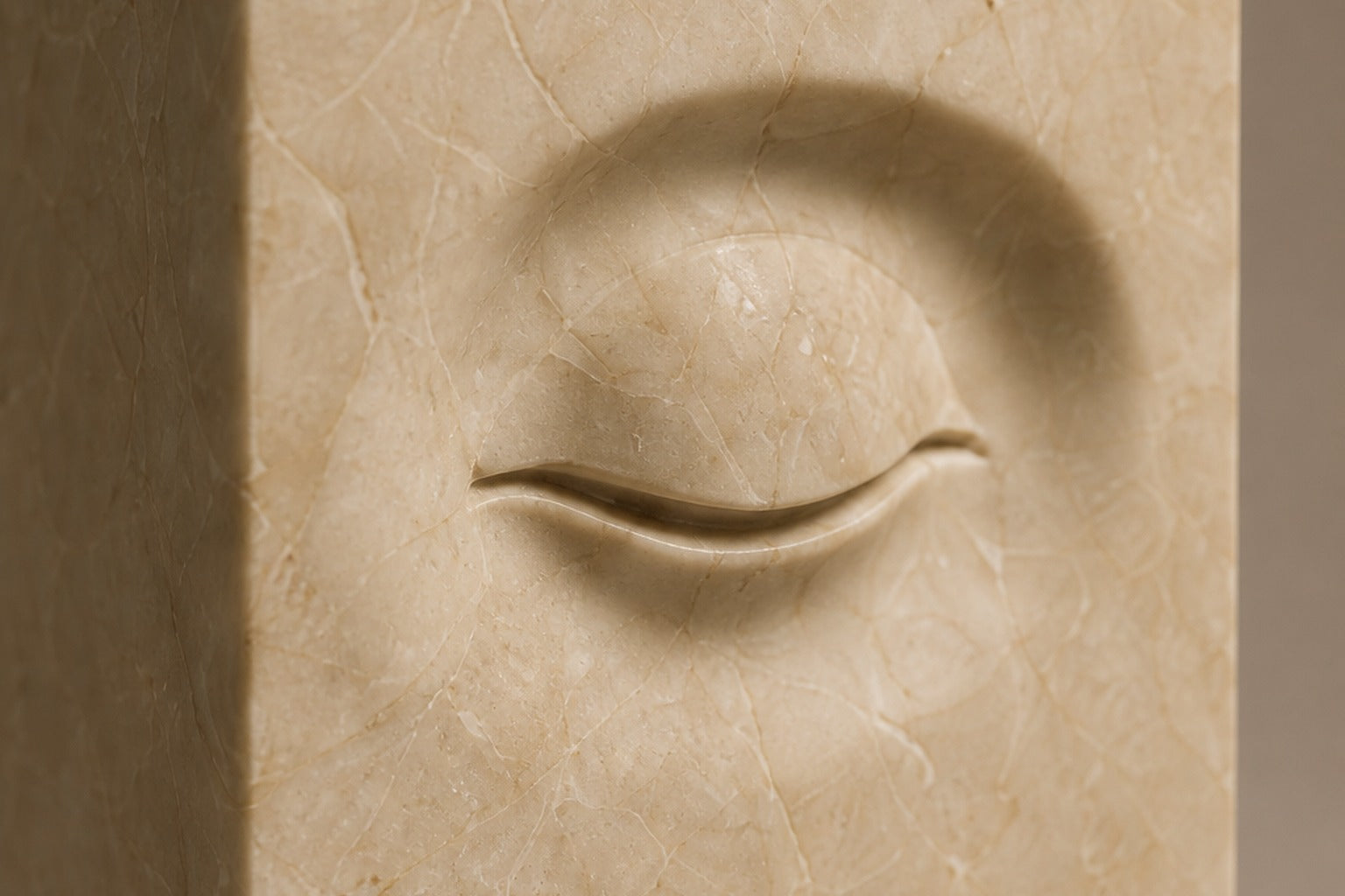 Tall cream Crema Marfil marble pedestal with a closed eye carved in shallow relief on one face.
