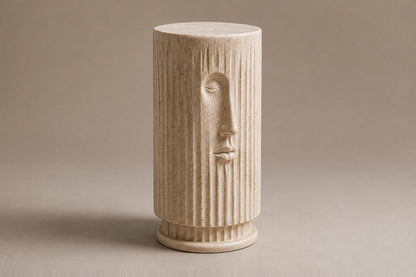 Fluted cream travertine drum on a round moulded foot, with a face carved through the flutes.