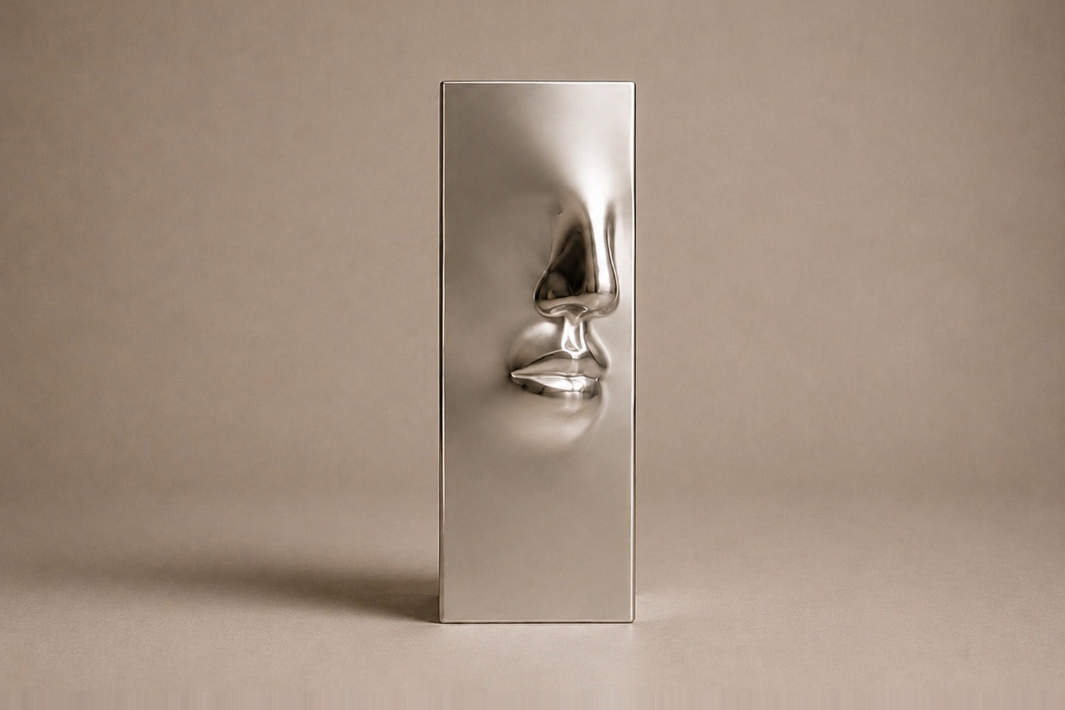 Tall mirror-polished stainless steel pedestal with a nose and mouth formed seamlessly out of one face.