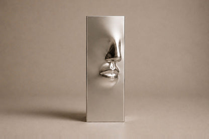 Tall mirror-polished stainless steel pedestal with a nose and mouth formed seamlessly out of one face.