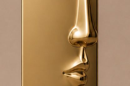 Tall gold PVD pedestal with a closed eye, nose and mouth formed seamlessly out of one face.