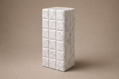 Tall white Carrara marble column carved into a grid of raised cushioned panels.