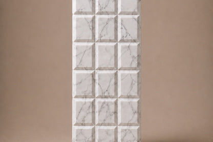 Tall white Carrara marble column carved into a grid of raised cushioned panels.