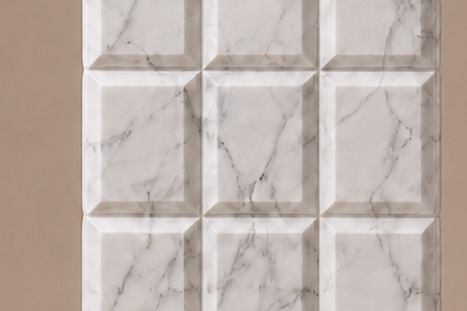 Tall white Carrara marble column carved into a grid of raised cushioned panels.