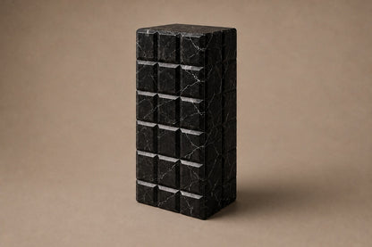 Tall black Nero Marquina marble column carved into a grid of raised cushioned panels.
