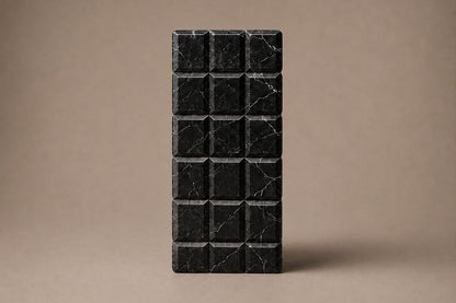 Tall black Nero Marquina marble column carved into a grid of raised cushioned panels.