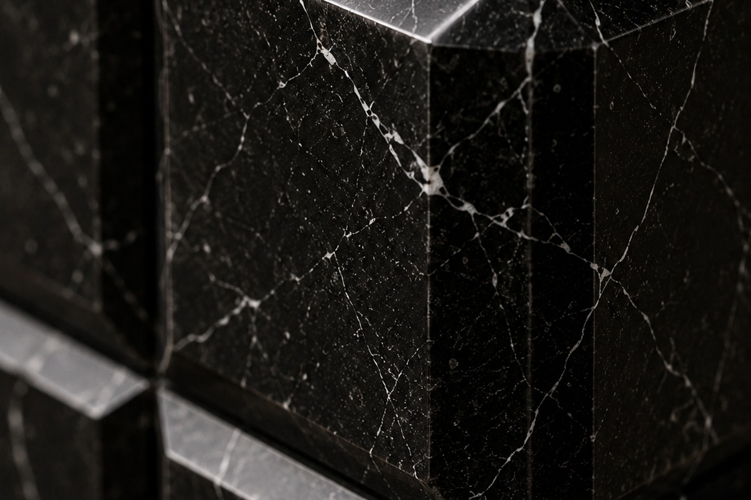 Tall black Nero Marquina marble column carved into a grid of raised cushioned panels.