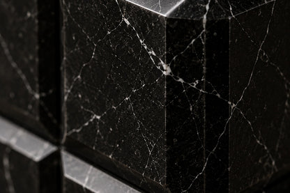 Tall black Nero Marquina marble column carved into a grid of raised cushioned panels.