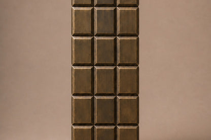 Tall antique bronze column built as a grid of raised cushioned panels.